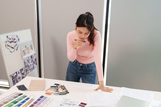 Asian Young Interior Designer Working on UI Project Floor Plan Color Swatches at Desk Creative Process for Home Renovation Design in Workplace