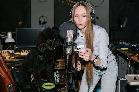 A black poodle and his mistress recording music in a music studio.