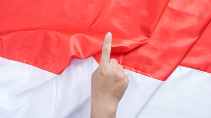 A hand making a gesture with the index finger pointing upward symbolizes number one or unity in front of the red and white Indonesian flag to celebrate Indonesia independence day