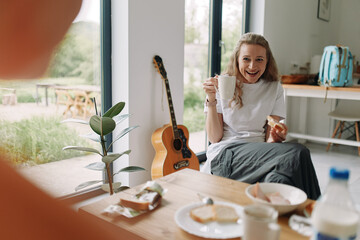 middle age woman enjoying healthy breakfast holding coffee cup in bright kitchen with natural light...