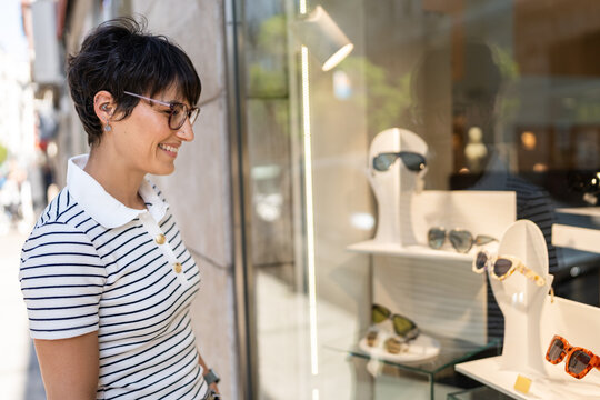 Smiling woman viewing eyewear in a shop window