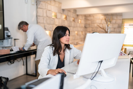 Female optician using computer in optical store with colleague working