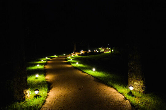 Dimly lit outdoor walkway at night with small garden lights softly illuminating the concrete path, creating a tranquil and inviting evening atmosphere.
