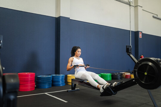 Young Latina using rowing machine during gym workout