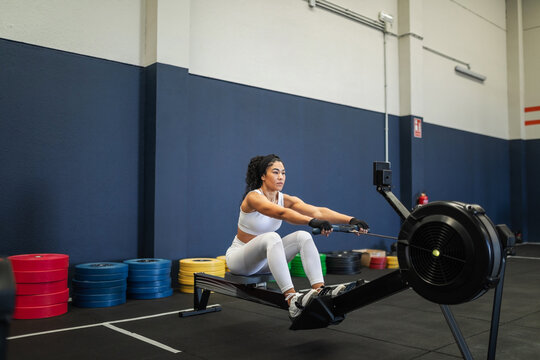 Young Latina using rowing machine during gym workout