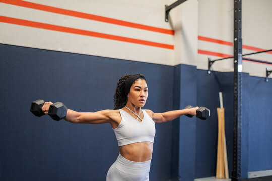 Young Latina doing lateral raises with dumbbells at the gym