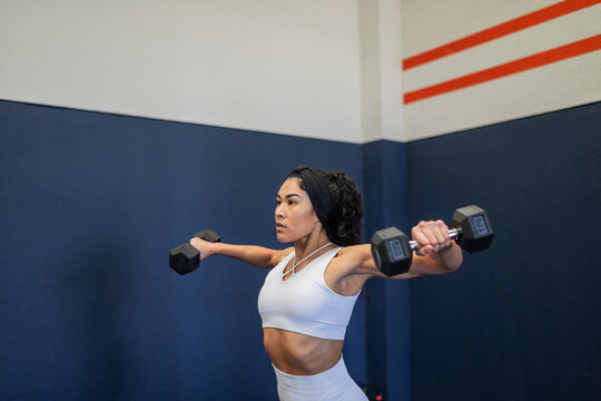 Young Latina doing lateral raises with dumbbells at the gym