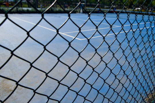 Close-up View of Metal Fence with Blue Tennis Court Background