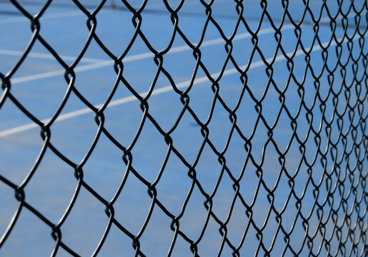 Close-up View of Metal Fence with Blue Tennis Court Background