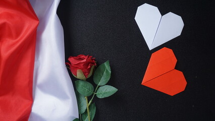 Crumpled red and white Indonesian flag with a rose and two heart shaped origami isolated on black background