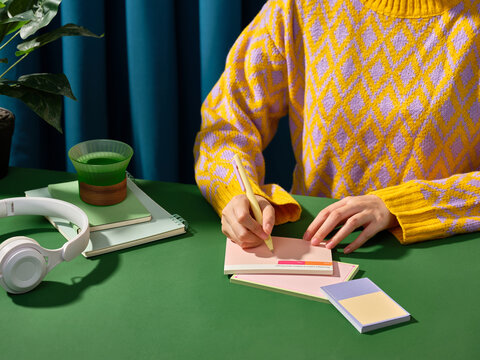 A person in a yellow sweater writing on a notepad