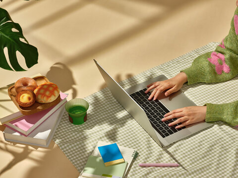 Hands working on a laptop beside food and drinks