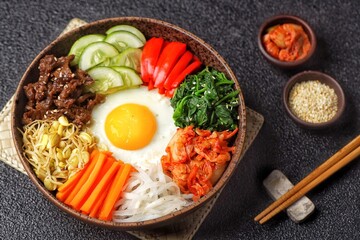 Bibimbap is a Korean dish in the form of a bowl of white rice topped with side dishes of vegetables, beef, eggs and spicy gochujang sauce.