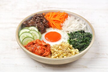 Bibimbap is a Korean dish in the form of a bowl of white rice topped with side dishes of vegetables, beef, eggs and spicy gochujang sauce.