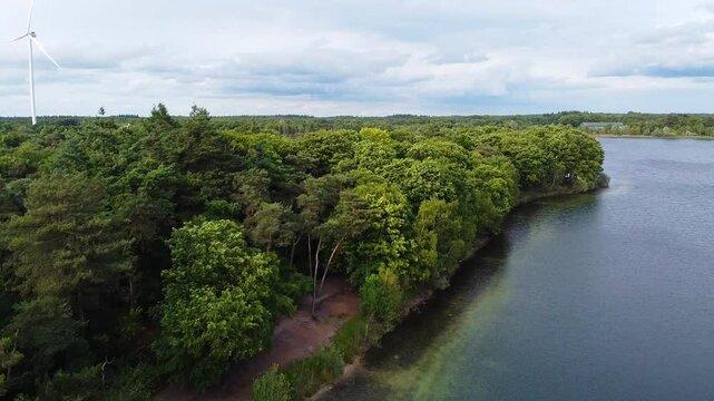 Aerial above scenic landscape with a lake and trees in near Breda, The Netherlands. windturbine and clouds in the distant horizon.