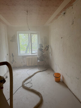 Worker sanding wall in dusty renovation interior