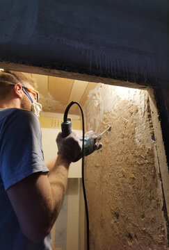 Worker using power chisel on old plaster wall