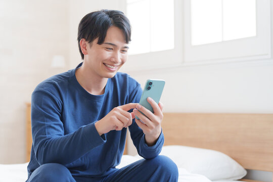 寝室でスマホを使う男性 - Powered by Adobe
