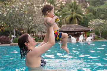 Caucasian woman holds her son while swimming in a pool on vacation. Mom teaches little boy to swim. 