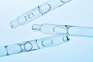 Several glass pipettes with liquid on gradient blue backdrop. 