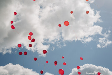 Red balloons float against a blue sky with white clouds