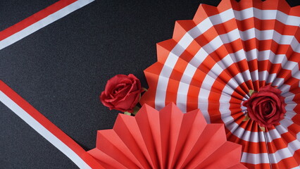 Independence Day Indonesia banner mockup with a rose, Indonesia flag color paper fans, and ribbons isolated on black background