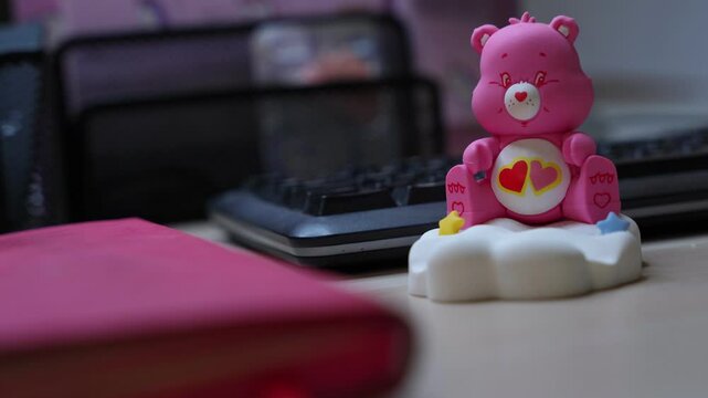 Cute pink bear toy on cloud in cozy workspace&mdash;great for themes of nostalgia, childhood, creativity, or playful desk decor.