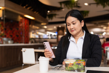 Woman in restaurant having salad and using phone