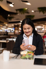 Woman in restaurant having salad and using phone