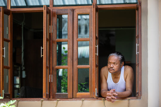 Elderly man leaning at window, deep in thought and quiet reflection