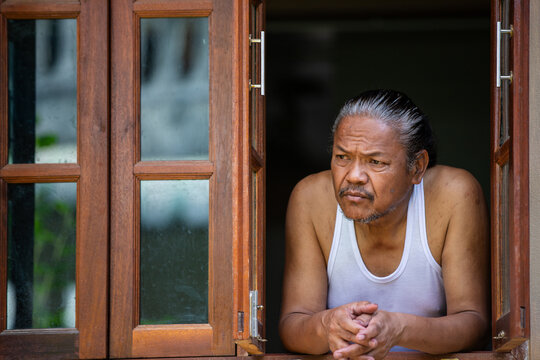 Elderly man leaning at window, deep in thought and quiet reflection