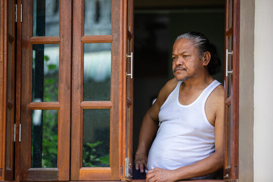 Elderly man leaning at window, deep in thought and quiet reflection