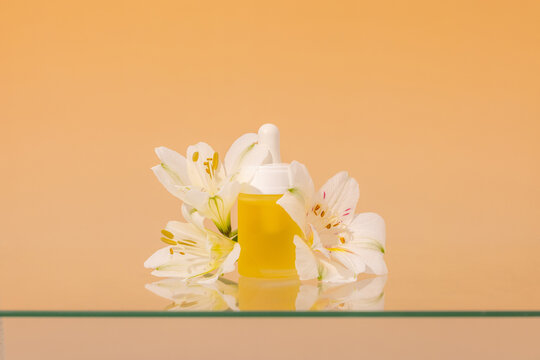 Bright orange serum bottle surrounded by white flowers on glass