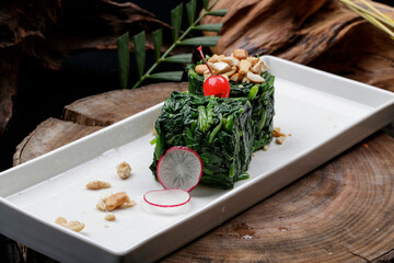 Rectangular porcelain plate of spinach rolls on a camphorwood chopping board