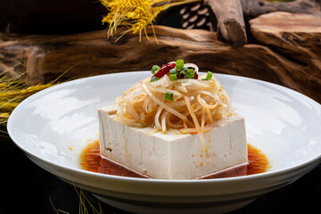 A round porcelain plate of tofu on a black background