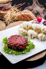 A rectangular porcelain plate of steamed buns with marinated meat is placed on a camphorwood chopping board.