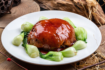 Braised pork belly in a round porcelain plate placed on a camphorwood chopping board
