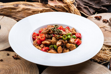 Spicy roasted rooster in a white round plate on a camphorwood chopping board