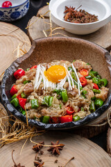 Fried beef with millet and chili sauce in a ceramic dish on a camphorwood chopping board