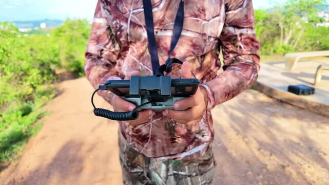 Close-up of drone operator holding a remote controller with phone display, outdoors tropical greenery.