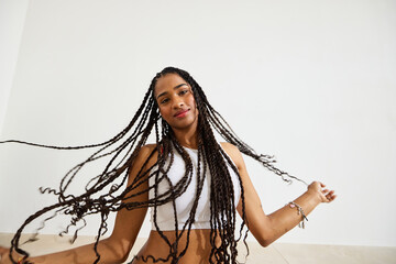 Woman joyfully showcasing her long braided hair in indoor settin