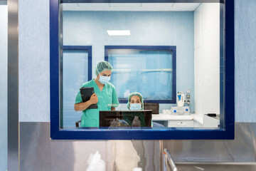 Medical team working on computer behind glass in operating room