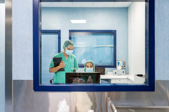 Medical team working on computer behind glass in operating room