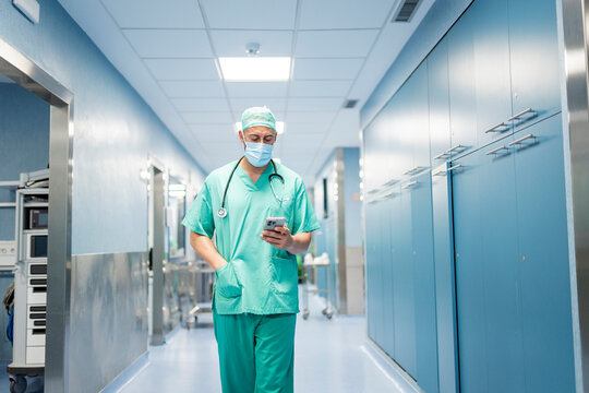 Surgeon wearing surgical mask and scrubs using cellphone in hospital.