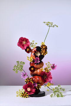 Stacked tomatoes and bright flowers create an artistic composition.