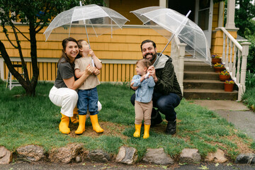 family playing in the rain with umbrellas, infant of their house 