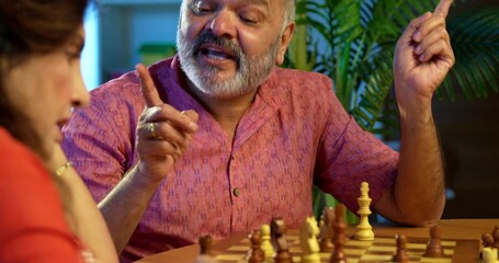 Senior couple playing chess board game at home, Indian retired husband wife enjoying strategic shatranj match while sitting at table, indoor recreation, family bonding, leisure, love concept - Powered by Adobe