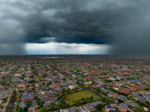 Heavy rain falling from dark storm clouds ofe suburban housing