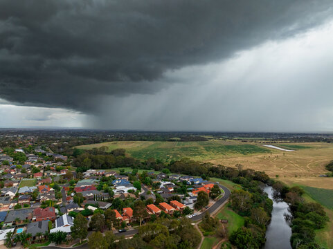 Heavy rain falling from dark storm clouds ofe suburban housing