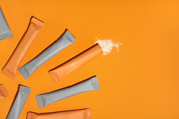 Sachets with collagen and vitamins in powder form on orange background
